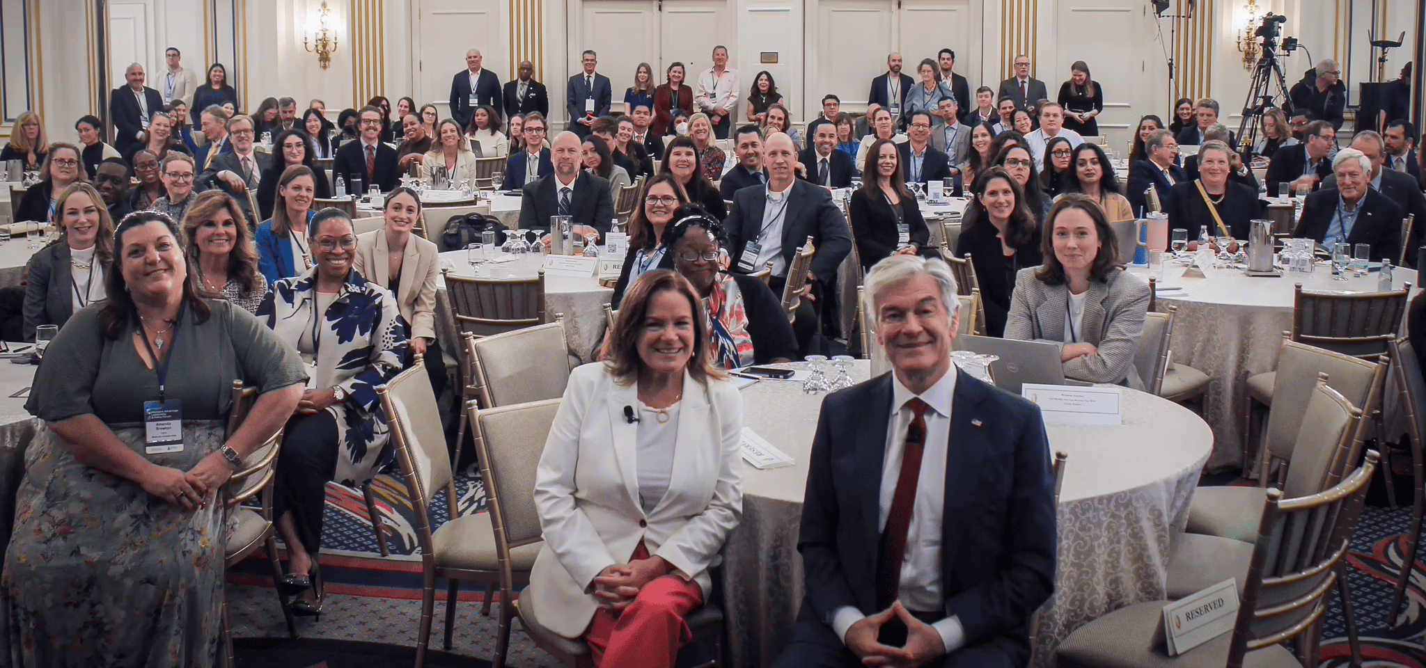 Large group of people in hotel ball room at a conference with Dr. Oz at the center